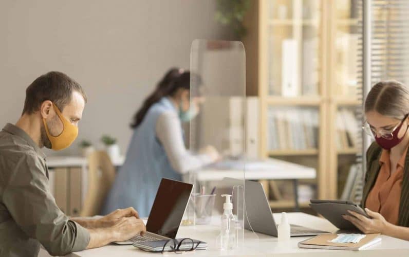 Personas trabajando en una oficina con mascarillas y pantallas de protección
